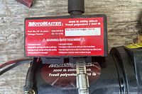 Close up of the red label on motor showing MotoMaster brand and 3000 lb capacity, voltage 12V DC, part and date codes with safety warnings.