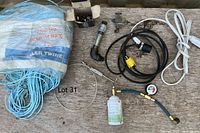 Overview photo showing large coil of blue binder twine, several extension cords with plugs, AC stop leak canister with pressure gauge and attachments on a wood surface.