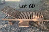 Reclining wooden sun lounger showing angled backrest and built-in sliding table extended, outdoors on gravel surface.