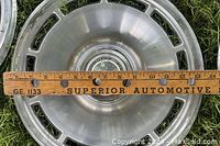 Close-up of one aluminum rim showing 14-inch diameter measured with a wooden ruler and featuring a metallic center cap with a 'Motor Wheel' logo.