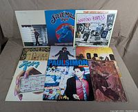 Nine vinyl records laid out showing front album covers by various artists including Steve Miller Band, Joe Cocker, Paul Simon, and others.