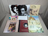 Front view of nine vinyl records by Joe Cocker, Lindsey Buckingham, Elton John, Pete Townsend, James Taylor, Quicksilver, The Mamas and The Papas, Linda Ronstadt, and The Hollies.