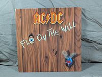 Front cover of AC/DC Fly on the Wall vinyl LP showing wood plank design with fly and eye graphics.