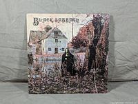 Front cover of Black Sabbath self-titled LP album showing woodland, house, and figure.