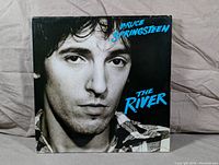 Front album cover featuring a close-up black and white photo of Bruce Springsteen with title text The River in blue.
