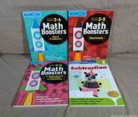 Front covers of four Kumon math workbooks including Math Boosters Word Problems (Grades 3-6), Math Boosters Decimals (Grades 3-5), Math Boosters Problems Solving with Ratios & Proportions (Grades 3-6), and Subtraction Level 1 workbook.