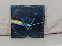 Front cover of Pink Floyd Dark Side of the Moon LP showing the iconic prism with a rainbow light beam on a dark background. The cover has visible wear and edge scuffing.