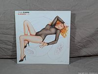 Front cover of 'Candy-O' album by The Cars showing a woman in a black bodysuit reclining on a car illustration.