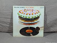 Front cover of Let It Bleed LP album with colorful layered cake and record player artwork, some signs of wear visible.