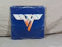 Front cover of Van Halen I album showing winged VH logo on blue background with wear around edges.