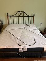 Front view of Queen size bed frame featuring decorative black metal headboard with wood posts and the white geometric patterned iComfort mattress with adjustable sections visible. Remote control placed on mattress.