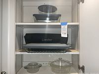 Shelf with multiple baking dishes including a large metal pan, wire rack, round glass baking dishes with lids, and black Anchor to-go bag.