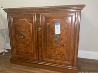 Front view of the closed bar console cabinet showing wood-grain paneled doors with ornate metal handles and a badge indicating lot number 10.