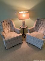 Full view of the pair of matching swivel chairs, ceramic lamp with matching fabric lampshade, and small side table with vintage doilie.