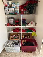 Cabinet with shelves displaying multiple Christmas decoration items including lights, hats, ornaments, and decorative plants.