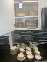 Full view of kitchen cabinet open with plates and bowls stacked inside, and cups and additional items on counter.