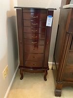 Front view of the closed wooden jewelry chest with eight drawers and two side doors. Chest stands on curved legs with polished dark wood finish.