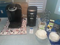 View showing Keurig coffee maker and Hamilton Beach BrewStation coffee maker on table with floral mat.