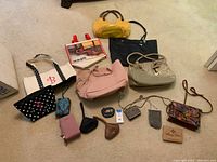 Photo of 14 assorted women's handbags, totes, clutches, and evening bags in various colors and styles on a beige carpeted floor.