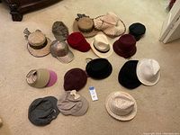 Wide shot of 17 different ladies hats arranged on carpeted floor showing a variety of styles and colors.