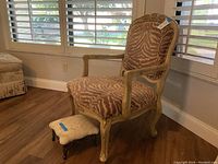 Accent chair with carved wooden frame and animal print upholstery, with a small decorative foot stool in front.