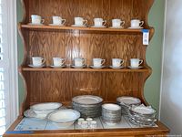 Wide view of china set displayed on wooden shelving showing cups, saucers, plates, bowls, and serving pieces
