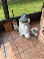 Four decorative patio items on tiled floor: turtle plant stand, cat statue, Kokopelli wall art, and wooden buoy.