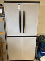 Front view of tall plastic storage cabinet with four doors and black vertical handles.