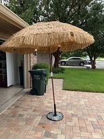 Full view of tiki umbrella set up on patio showing natural thatched canopy and wooden pole.