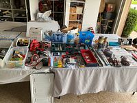 Full view of the garage table with hand tools, paints, bulbs, and utility items arranged