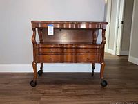Front view of the cherry wood vintage convertible table showing two drawers and castor wheels.