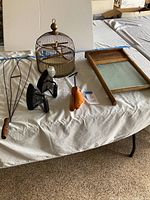 Overall view of vintage items including birdcage, two cast irons, wooden rug beater, shoe stretcher and washboard on table.