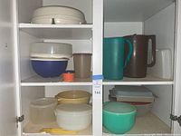 Wide view of white kitchen cabinet shelves displaying various vintage Tupperware containers and pitchers.