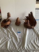 Three wood decor sculptures displayed on a white cloth with a plain white background.