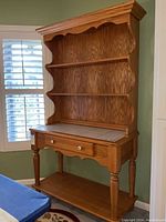 Front view of wooden baker's rack with decorative tile countertop, drawer, scalloped side shelves, and lower shelf.