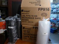 Full view of stacked black containers and white lids next to cardboard boxes for the lot.