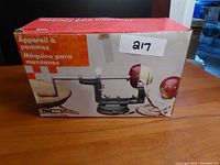 Front of the box showing Apple Machine branding and image of the device peeling an apple with suction base on a table