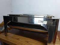 Side view of the full-size stainless steel rectangular chafer showing its legs and tray.
