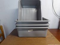 Stacked four gray plastic buster bins on a wooden table against a white wall