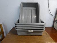 Stack of 5 gray plastic buster bins on wooden table against a white wall