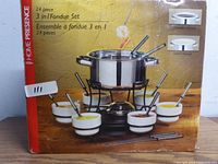 Box photo showing Home Presence 24 piece 3-in-1 fondue set with stainless steel pot, ceramic bowls, forks, stand and gel fuel holder.