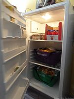 Open door view of the white Kenmore upright refrigerator showing interior shelves, door bins, and light with some grocery bags inside removed for sale.
