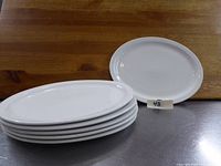 Photo of six white oval porcelain plates stacked with one plate upright, showing clean smooth surface and sizes.