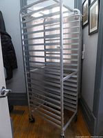 Side angled view of the 20 shelf metal baker's rack showing its metal frame, shelf slots and rolling casters.