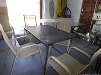 Photo showing rectangular metal mesh outdoor table with 4 cream vinyl mesh chairs around it.