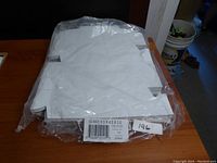 Photo of the sealed package of flat white paper take out containers stacked on a wooden table.