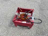 Red metal framed propane stove with circular burner and hose connected, placed on asphalt surface
