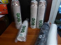 Five plastic-wrapped bundles of food containers and lids on a table - four bundles of white paper food containers each with 50pcs and one bundle of lids in black and white.