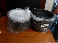 Plastic containers with black bases and clear round lids stacked and packaged in plastic wrap, approximately 50 pieces total.