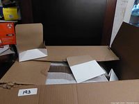 Open cardboard box with many flat-packed paper containers inside, one container partially folded showing white interior and brown exterior